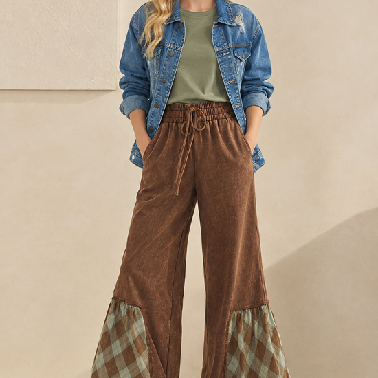Styled outfit featuring brown plaid-trim wide-leg pants, a sage green T-shirt, a distressed denim jacket, and cream sneakers.