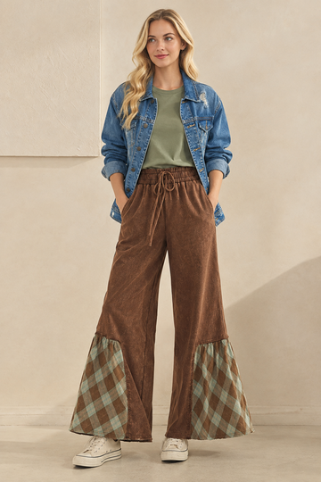 Styled outfit featuring brown plaid-trim wide-leg pants, a sage green T-shirt, a distressed denim jacket, and cream sneakers.
